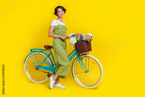 Full body photo of cute young lady girlish bicycle shopping promo 8 march dressed stylish khaki garment isolated on yellow color background © deagreez