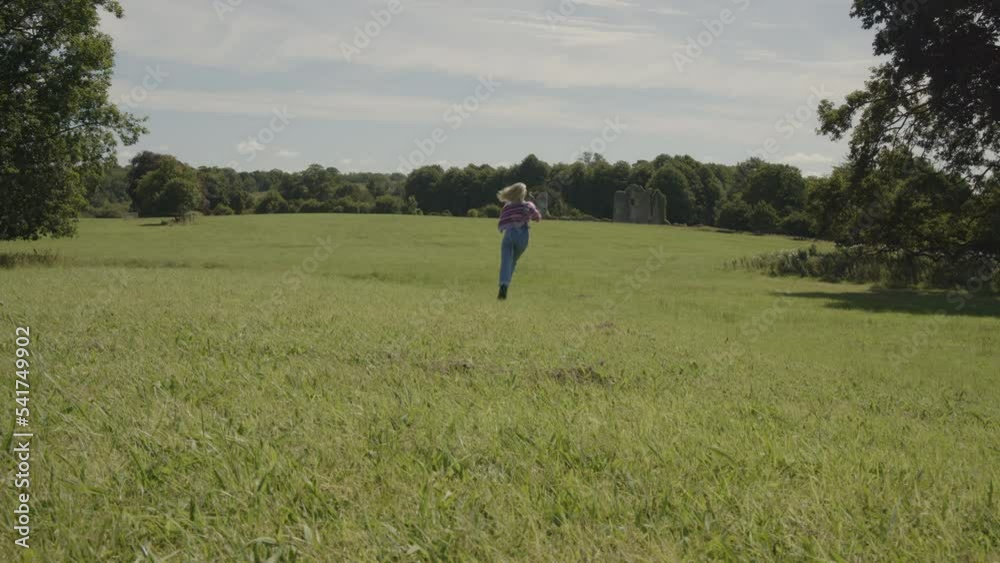 Surface level view of carefree woman running away in field / Enniskillen, Northern Ireland Surface level view of carefree woman running away in field / Enniskillen, Northern Ireland