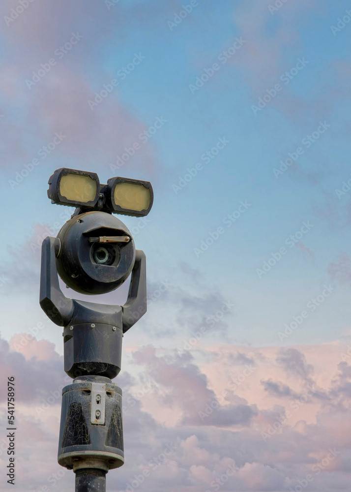 Vertical Puffy clouds at sunset Moving security camera on a post with lights on top