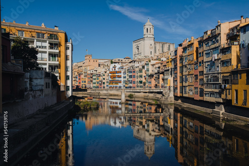 Girona, Spain on 22 October 2022: Colorful yellow and orange houses in historical jewish quarter of Girona, Catalonia, Spain reflecting on the Oñar river with clear blue sky photo