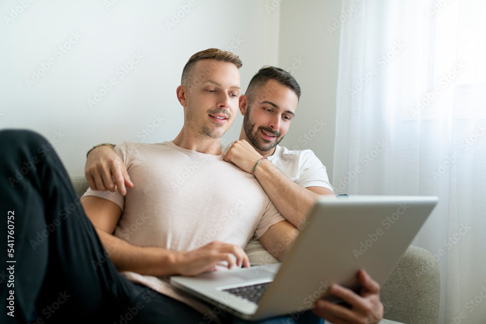 Happy young two man couple using laptop computer while sitting on a couch at home Happy young two man couple using laptop computer while sitting on a couch at home