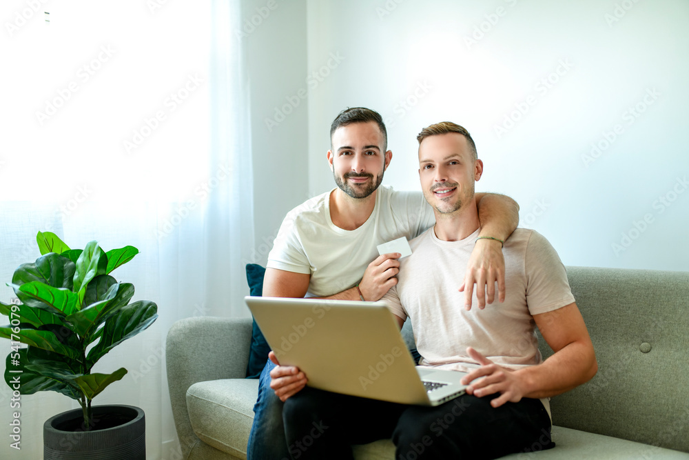 Happy young two man couple using laptop computer while sitting on a couch at home Happy young two man couple using laptop computer while sitting on a couch at home