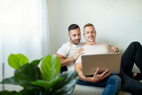 Happy young two man couple using laptop computer while sitting on a couch at home