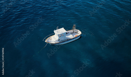 Aerial view of a little fishing boat at dawn surrounded by a crystalline deep blue sea moored in Calabria, Italy. photo
