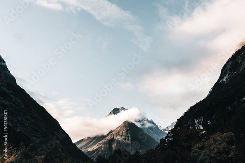 stunning landscape of calm snowy big rocky mountain tops among clouds and blue sky, milford sound, new zealand