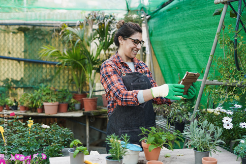 Happy latin woman working inside greenhouse garde while using digital tablet