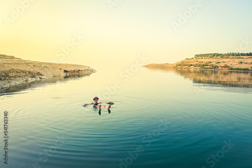 Caucasian female tourist float on dead sea water happy enjoy vacation in Jordan. Sunset panorama with person in salty lake water