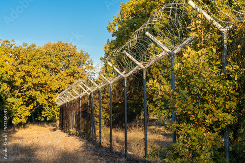 view of a tall fence with barbed wire leading through forest on the border of Turkey and Bulgaria
