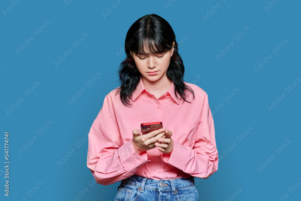 Sad female looking at smartphone screen, on blue color background Sad female looking at smartphone screen, on blue color background