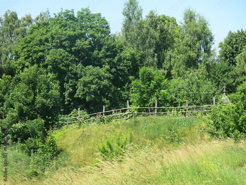 picturesque cliff above the river in summer with a wooden rural fence