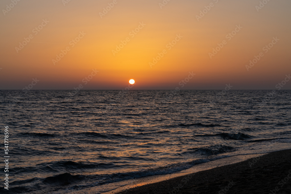sunset on the Mediterranean Sea in Greece with calm ocean water and dark sand beach in the foreground