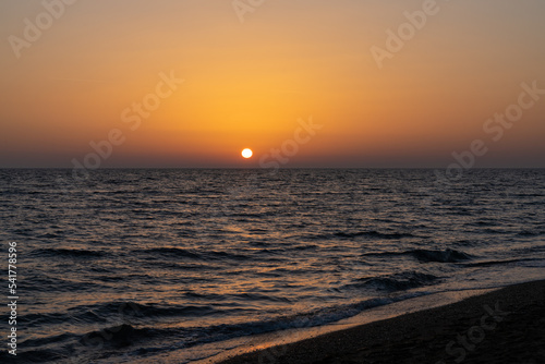 sunset on the Mediterranean Sea in Greece with calm ocean water and dark sand beach in the foreground