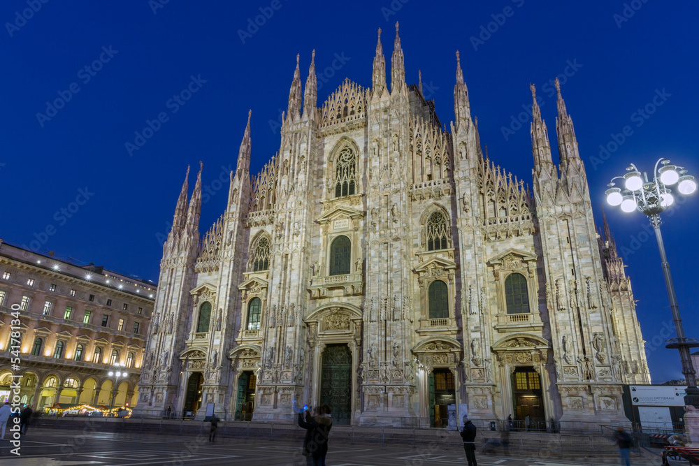 Duomo, the famous cathedral of Milan, Italy, during blue hour in late afternoon. At the left background it's the Galleria Vittorio Emanuele, Italy's oldest shopping gallery.