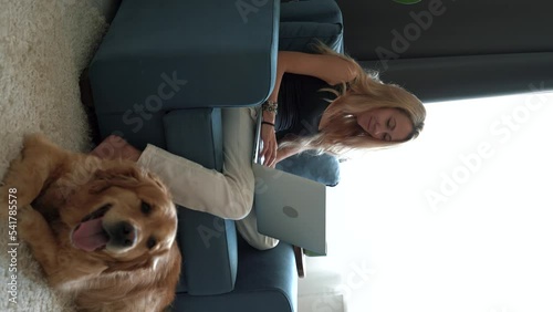 Smiling young beautiful woman sitting with her pet dog using laptop while working from home. Vertical shoot. 4k footage
