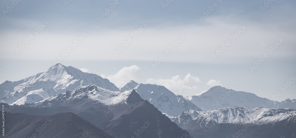 Panoramic view of mountain range, hills and peaks with snow and unusual clouds, monochrome landscape with cloudy sky