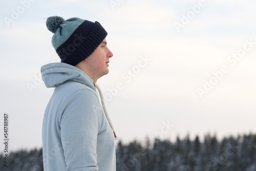 Handsome guy, young relaxed man is breathing deep deeply fresh air outdoors at winter snowy cold frosty day standing on top peak of mountain in forest on natural background. Copy space, place for text