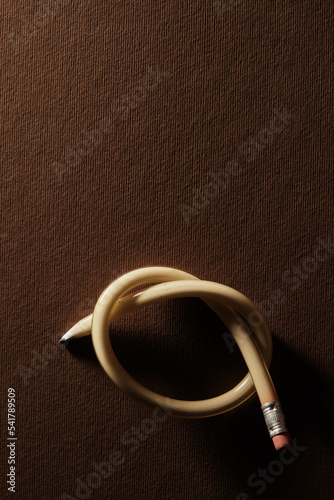 rubber-y pencil tied into a large knot. The pencil is orange and against abrown background photo