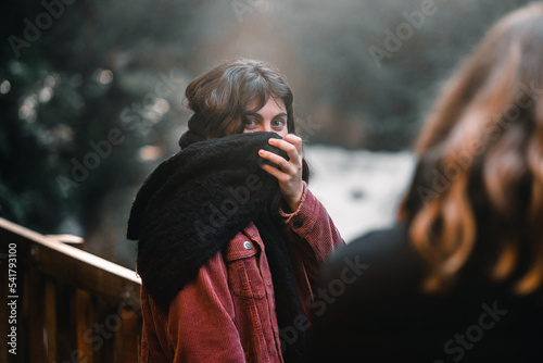 blue-eyed caucasian young woman in red corduroy jacket covering her mouth with black woolen scarf on wooden gazebo near waterfalls amid nature and forest greenery, marian falls, new zealand photo