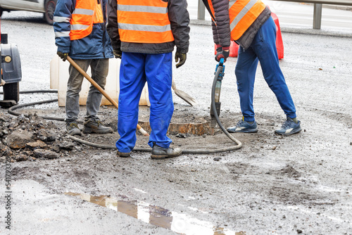 A repair team of road workers with a jackhammer and a shovel clears a sewer manhole for its repair on the road.