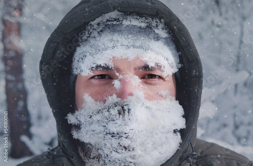 Man's face in the snow against the backdrop of a snowfall. Man in snow storm close up, snowy frosty winter