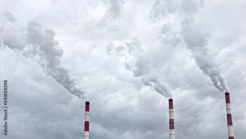 Industrial coal chimneys produce harmful chemical emissions. Thick smoke emits from energy factory floating across dark cloudy sky causing environmental pollution