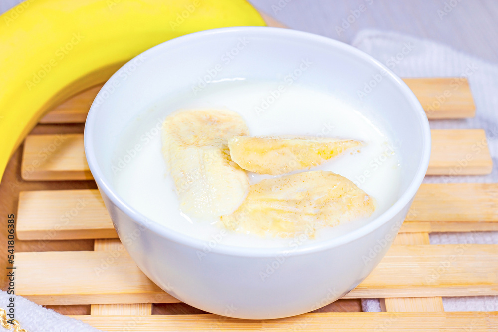 Banana slices in coconut milk in a white bowl on light wooden background. Banana slices in coconut milk in a white bowl on light wooden background.