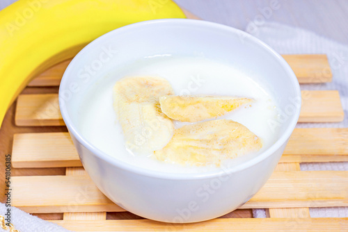 Banana slices in coconut milk in a white bowl on light wooden background.
