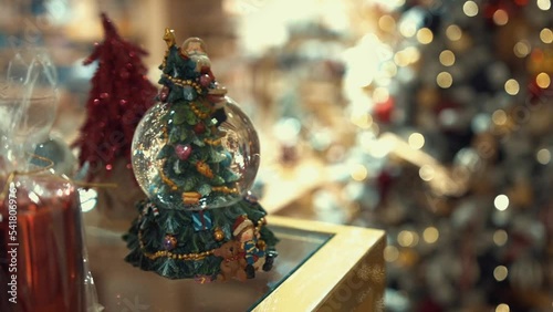 Buying Christmas presents for a family in a cozy shop, traditional holiday shopping in a trade center. Christmas tree decorated with artificial snow, shining lights, feathers, carnival-style tree toys