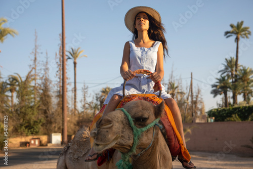 Canvas-taulu Sexy woman on a dromedary or camel with a hat in the desert of the palm grove of Marrakech in Morocco, this is a place very visited by tourists on vacation and fun