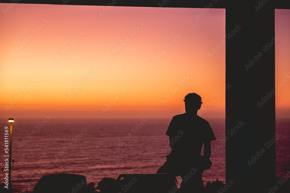 Silhouette of a person in a terrace in front of the beach with colorful sunset