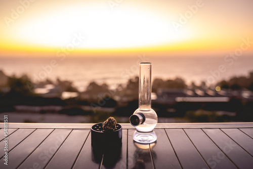 Marijuana bong (weed water pipe) and black grinder with big marijuana bud with beautiful sunset sky and sea