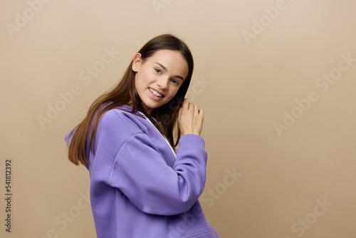 horizontal portrait of a beautiful, mischievous, happy woman in purple clothes on a beige background raising her hand to her head and smiling charmingly looking at the camera © Tatiana