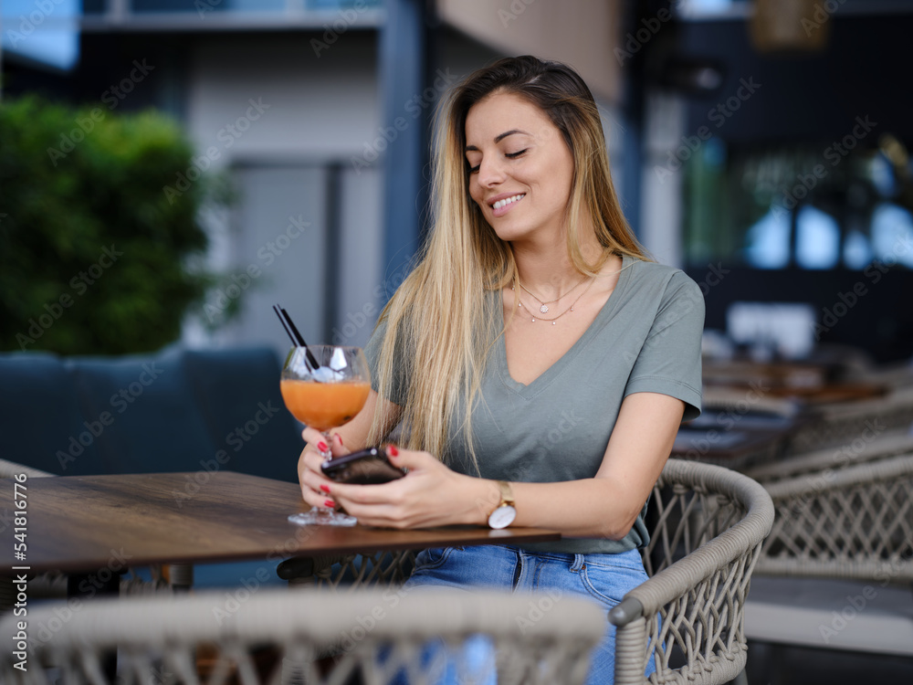 A happy young woman sits in a bar and drinks cocktail. Stock Photo ...