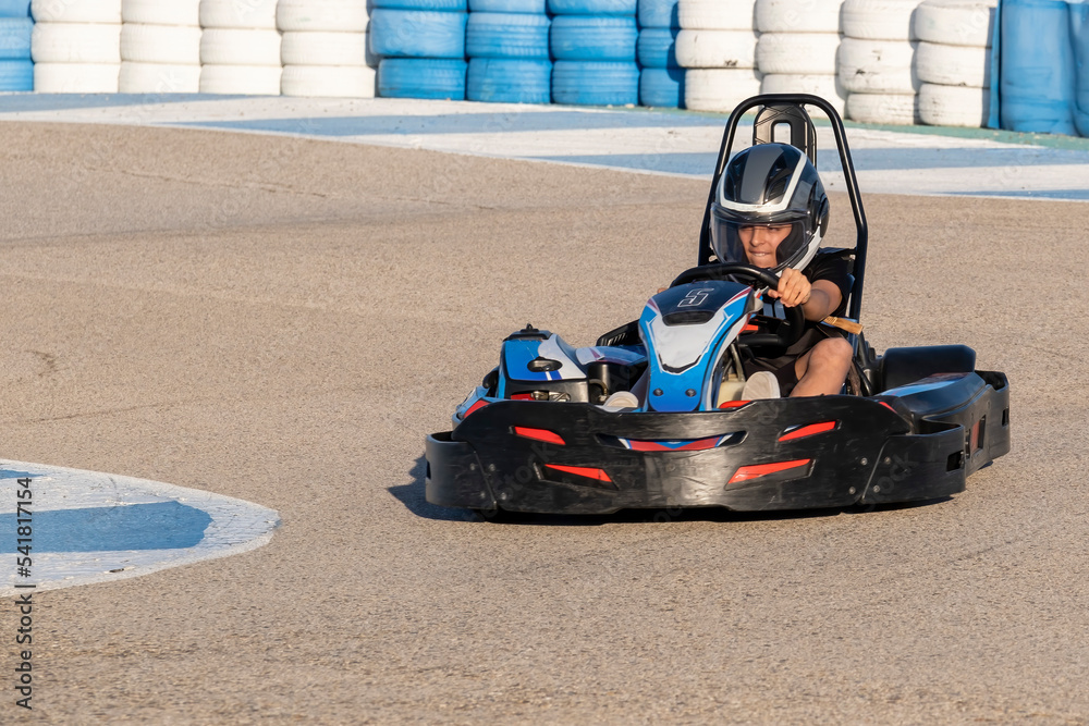 a teenager boy driving a kart at the exit of a curve of a karting circuit, face of speed and concentration while driving a go kart - obrazy, fototapety, plakaty 