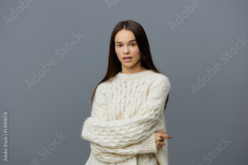 horizontal studio portrait on a gray background of a beautiful, refined, gentle woman in a white sweater smiling pleasantly at the camera with her arms crossed on her chest