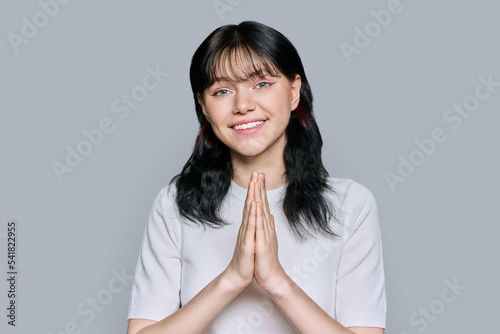 Young female pleading, holding hands in prayer on grey background