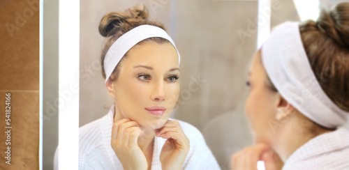 woman looking in the mirror in the bathroom and taking care of her skin.Applying the cream .Magic anti-aging cream.