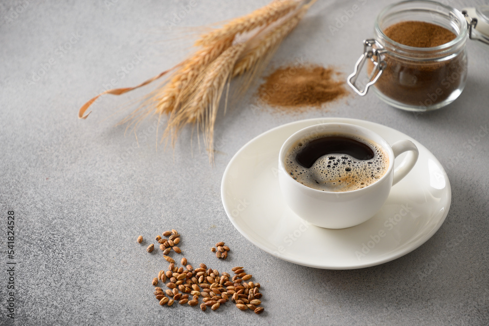 Barley coffee in white cup, beans and ears of barley on gray background