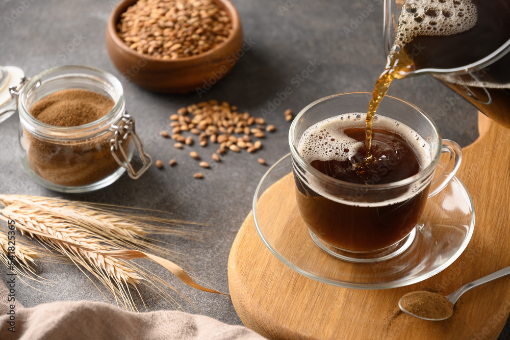 Pouring barley coffee in glass cup on brown background. Cooking healthy