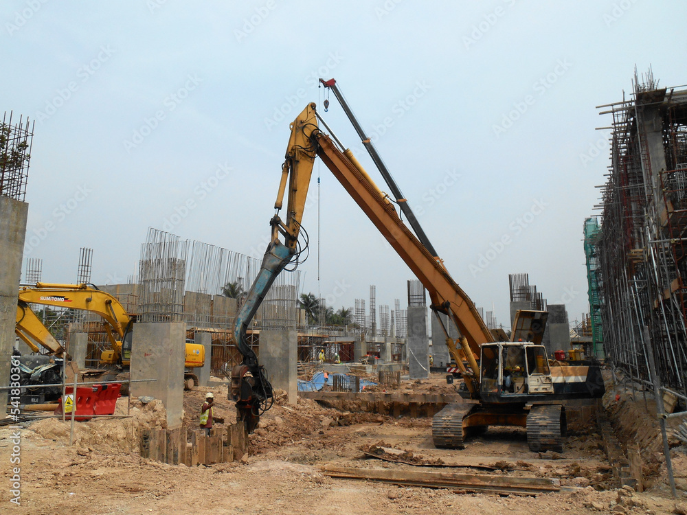 SELANGOR, MALAYSIA –MARCH 15, 2016: Sheet pile cofferdam driven machine at the construction site. The machine drove the sheet pile to the earth using vibrated hydraulic arm. Workers control. SELANGOR, MALAYSIA –MARCH 15, 2016: Sheet pile cofferdam driven machine at the construction site. The machine drove the sheet pile to the earth using vibrated hydraulic arm. Workers control.
