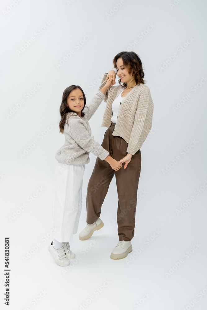 trendy girl looking at camera while holding hands with mom and dancing on grey background trendy girl looking at camera while holding hands with mom and dancing on grey background