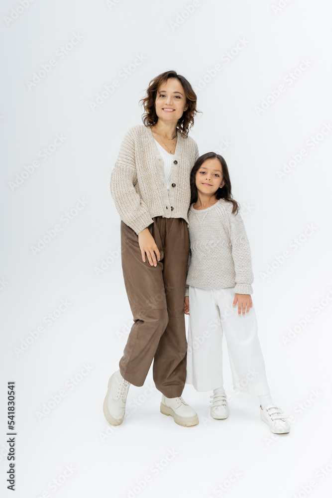 full length of mother and daughter in knitwear and pants posing on grey background full length of mother and daughter in knitwear and pants posing on grey background
