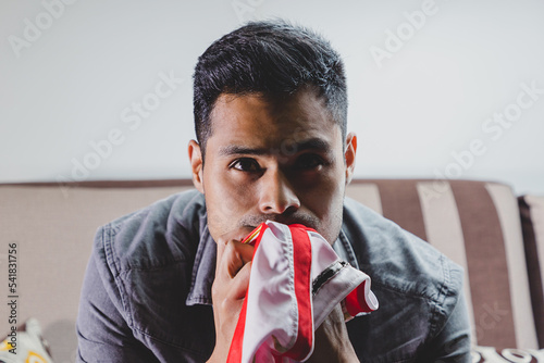 Joven fanático del fútbol, gritando gol, apoyando a su equipo sentado en el sofá de casa viendo la transmisión en vivo del encuentro. Concepto de mundial de futbol e hinchas del futbol en el mundo.