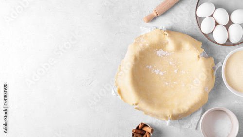 Raw crust pie dough into a baking dish with ingredient and rolling pin on a light gray background. Top view of homemade pie crust on the table. Home baking concept, pie crust recipe, hobby home bakery