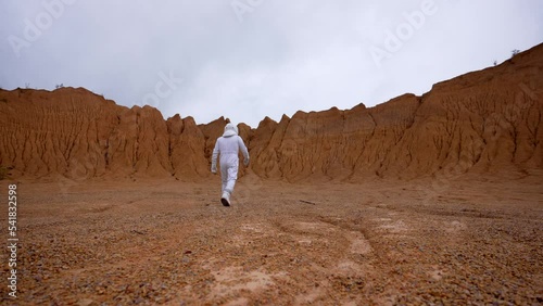 The astronaut walks along the surface of Mars to the border of the crater. Slow motion shooting and wide shotn of a man in an astronaut costume from the following samples of an unknown planet. photo