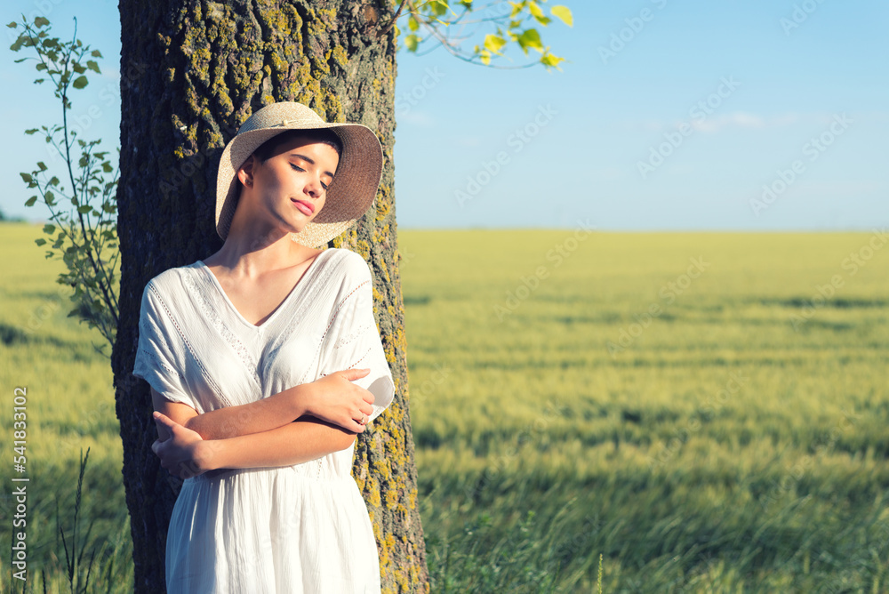 Young woman in white dress and hat walking in the wheat field on a ...
