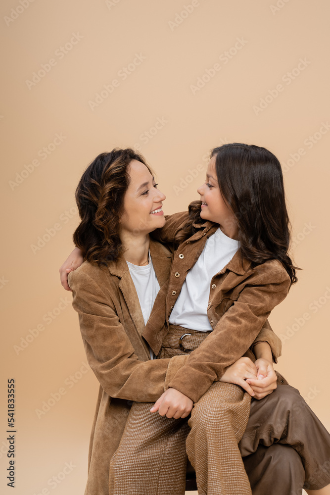 joyful mom and daughter in trendy autumn outfit looking at each other isolated on beige joyful mom and daughter in trendy autumn outfit looking at each other isolated on beige