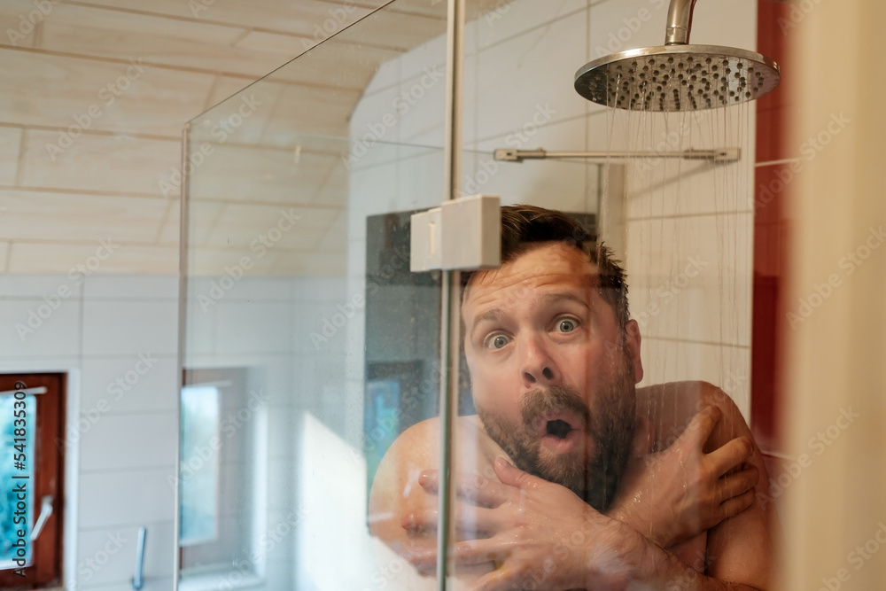 Man in the shower under cold water, freezes and hugs himself. Concept