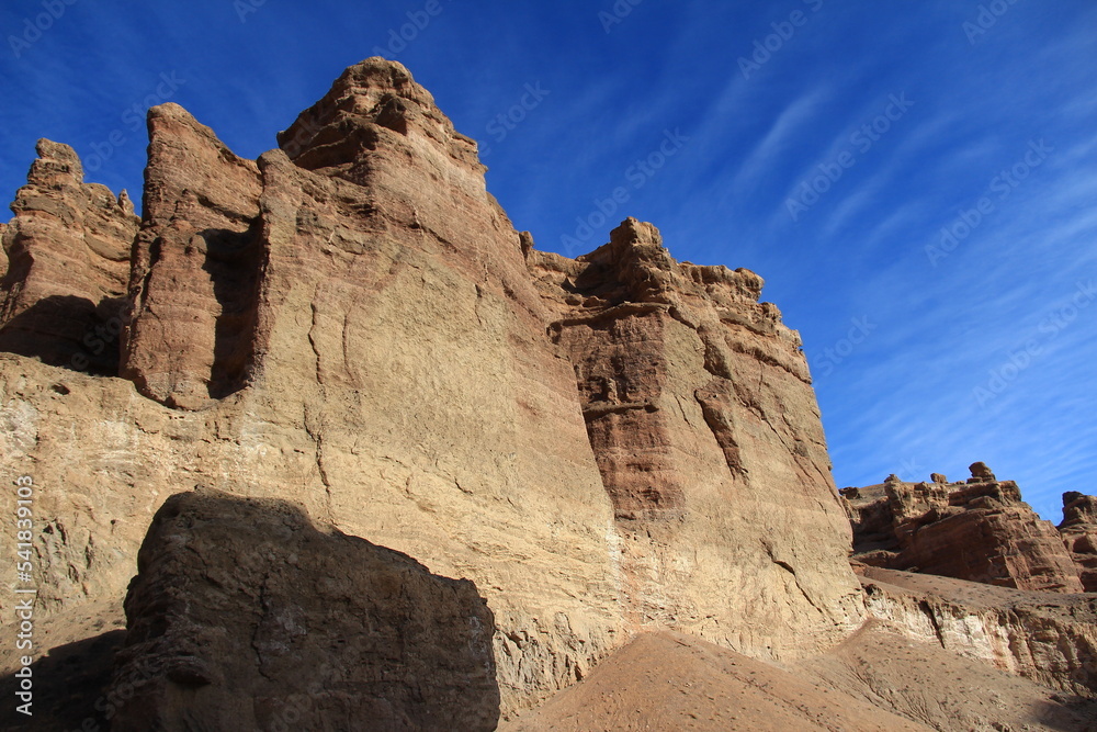 A huge sheer wall in the sandy-clay canyon of Charyn against the background of the sky with beautiful thin clouds in sunny weather
