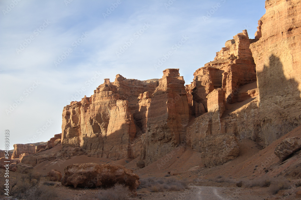 A wall of beautiful relief towers in the sandy-clay canyon Charyn against the background of a sky with clouds, sunny